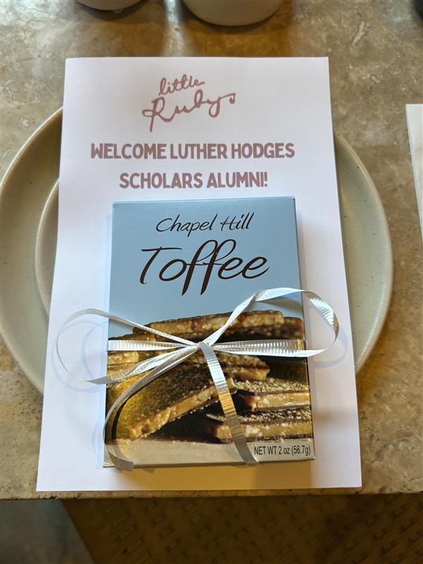 Photo of customized Welcome Luther Hodges Scholars Alumni "Little Ruby's" menu with Chapel Hill toffee on top